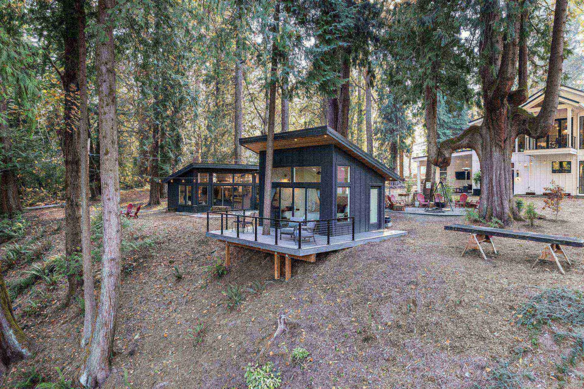 A modern cabin nestled among trees with a spacious deck area, perfect for gathering with friends or enjoying outdoor meals. The tranquil setting is ideal for relaxing after a day of exploration, reflecting the unique lodging experience described in the section.