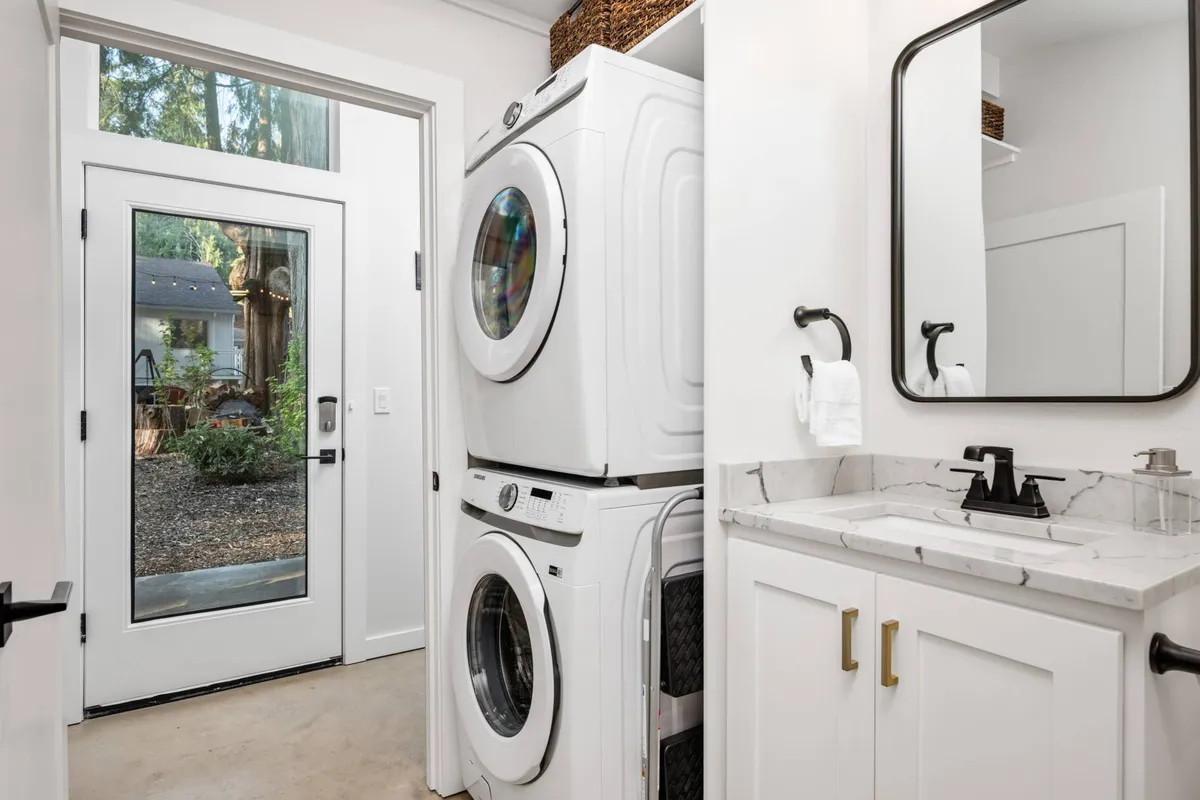 A practical and inviting laundry area featuring a washer and dryer, a vanity with a sink, and a door leading outside. The atmosphere is clean and organized, with a nod to convenience and everyday ease.